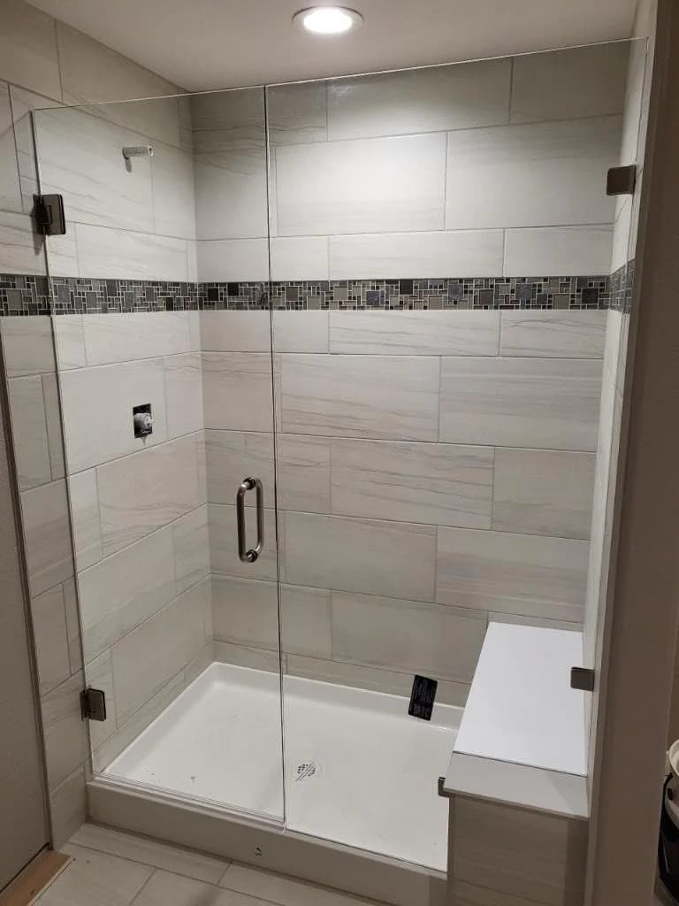Glass-enclosed shower with tiled walls and mosaic accent