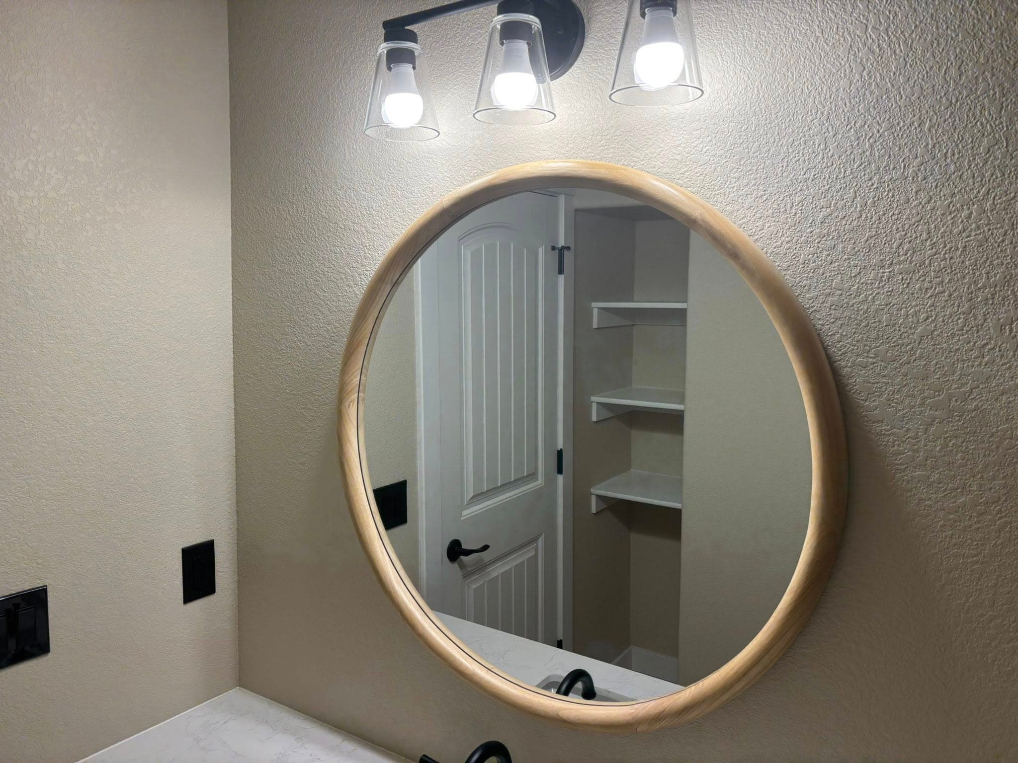Round wood-framed mirror and modern vanity lighting