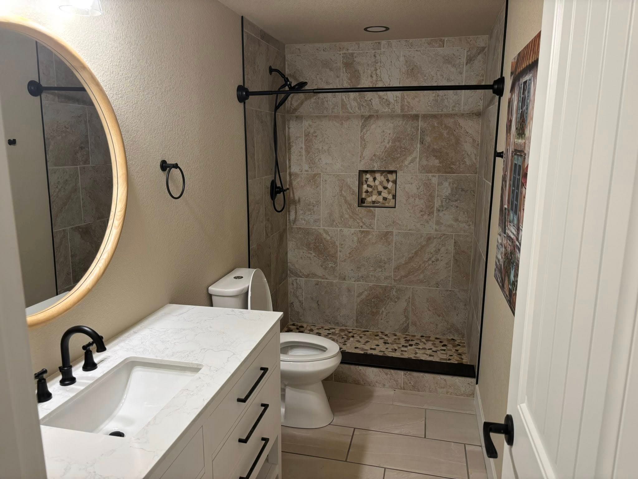 Walk-in tile shower with floating vanity and round wood-framed mirror
